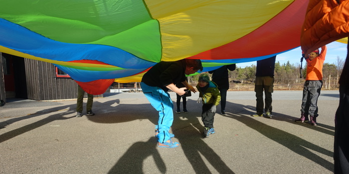 Far og sønn beveger seg under den fargerike fallskjermen som resten av gruppa holder oppe 